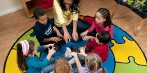 A teacher and students seated in a circle with hands outstretched toward the center.